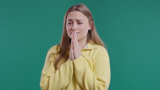Young woman praying, begs to apologize her, she is guilty. Blue background.