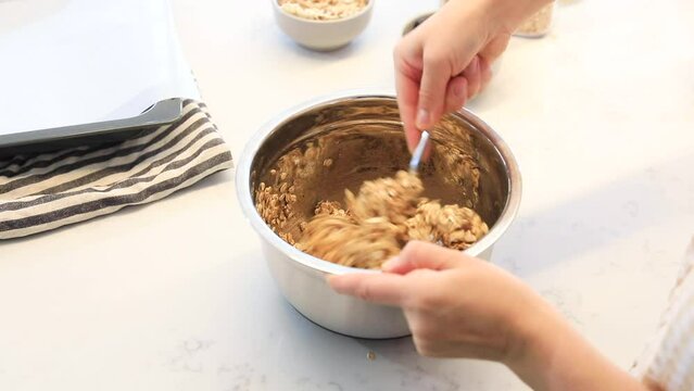 A woman mixes ingredients for homemade granola in a bowl. Video recipe, step 2