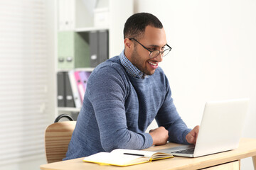 Naklejka premium African American man in glasses working on laptop indoors