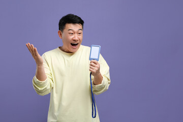 Emotional asian man with vip pass badge on purple background. Space for text