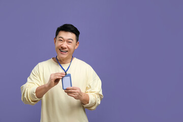 Happy asian man with vip pass badge on purple background. Space for text