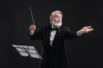 Professional conductor with baton and note stand on black background