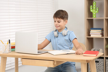 Boy with headphones using laptop at desk in room. Home workplace
