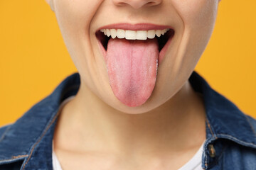 Happy young woman showing her tongue on yellow background, closeup