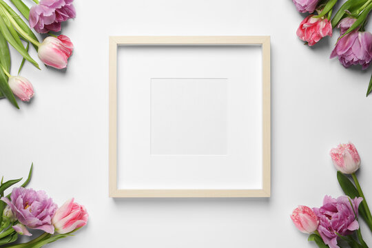 Empty photo frame and beautiful tulip flowers on white background, flat lay. Space for design