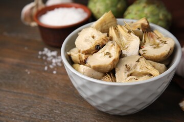 Bowl of pickled artichokes on wooden table, closeup