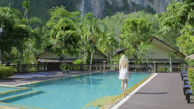 Influencer at Thailand resort walks barefoot in white dress next to resort pool