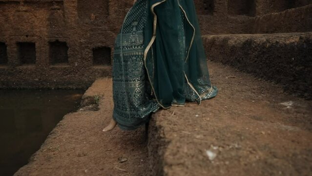 Closeup of indian woman in purple dress walking down earthen stone steps to historic pond