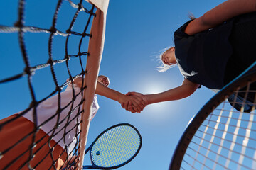 Two female tennis players shaking hands with smiles on a sunny day, exuding sportsmanship and friendship after a competitive match. - Powered by Adobe