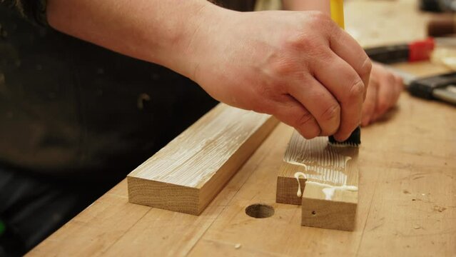 Carpenter spreads glue on wooden pieces using a brush in a woodworking studio. High quality 4k footage