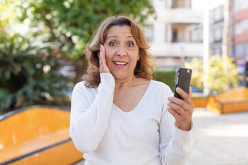 middle age pretty woman feeling happy and astonished at something unbelievable. using her smartphone