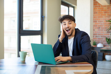 young handsome man feeling happy and astonished at something unbelievable. freelance concept with laptop