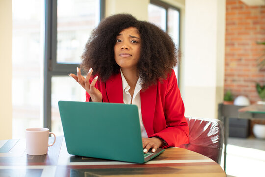 pretty afro black woman shrugging, feeling confused and uncertain. businesswoman and laptop concept