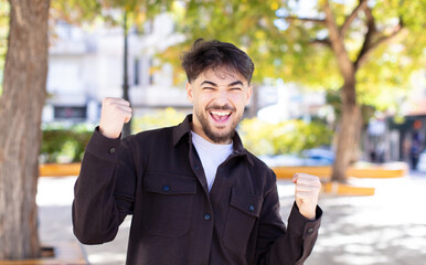 young handsome man feeling shocked, excited and happy, laughing and celebrating success, saying wow!