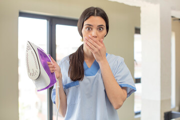 pretty young model covering mouth with a hand and shocked or surprised expression. housekeeper and laundry concept