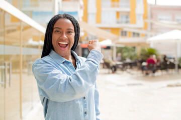 afro pretty black woman feeling happy, satisfied and powerful, flexing fit and muscular biceps, looking strong after the gym