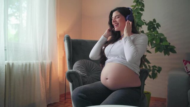 Beautiful young pregnant woman listening to music at home 