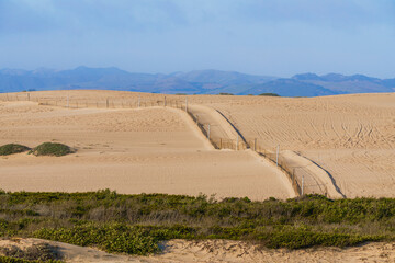 Sand dunes, silhouettes of mountains, and a cloudy sky in the background.  Oceano Dunes, California