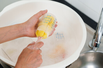 mother hand washing baby plastic milk bottle