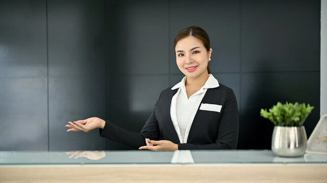 Friendly and attractive Asian female receptionist in a uniform stands at a front desk