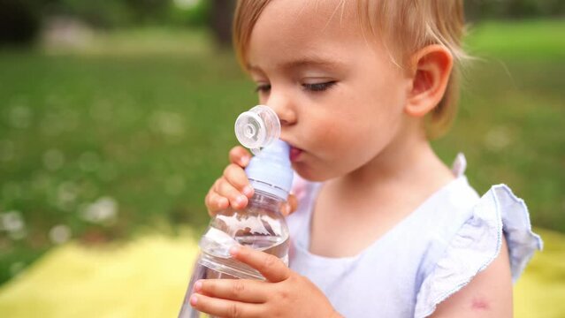 Little girl drinks water from a bottle with a non-spill cap