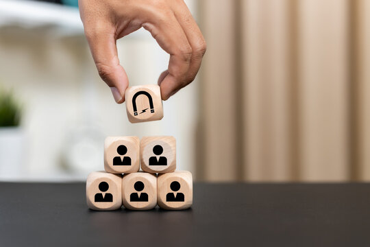 concept of marketing strategy customer attraction. Hand holding wooden cubes with magnet attracts and human icons on table office. Law of Attraction connections business partners marketing.