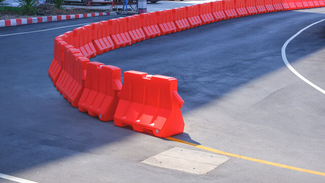 Row of orange plastic barriers on curve asphalt road in outdoor car parking area
