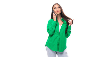 pretty young brunette woman with make-up in a green shirt speaks on the phone on a white background with copy space