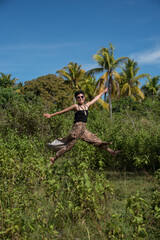 Happy female model jumping at the tropical location. Woman wears short black hair and sunglasses. Palm trees and blue sky on the background. Concept - tourism, travel, vacation, freedom.