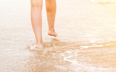 Close-up of female feet step on the sea wave and walking on sandy beach. Summer vacations concept.
