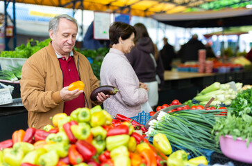 Aged man and woman customers buying pepper in open-air market
