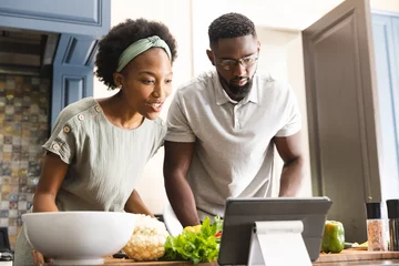 Tuinposter Focused african american couple preparing meal together using tablet in kitchen © WavebreakMediaMicro