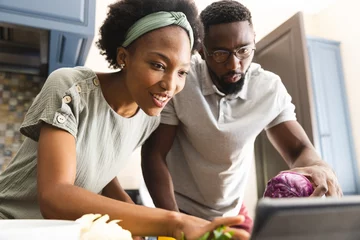 Tuinposter Happy african american couple preparing meal together using tablet in kitchen © WavebreakMediaMicro
