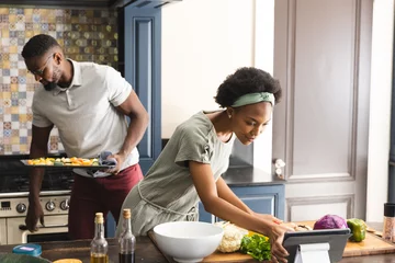 Tuinposter Happy african american couple preparing meal together using tablet in kitchen © WavebreakMediaMicro