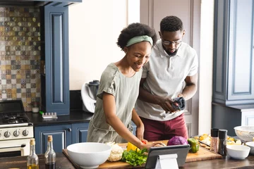 Fotobehang Happy african american couple preparing meal together using tablet in kitchen © wavebreak3