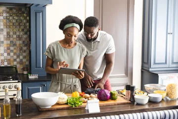 Fotobehang Happy african american couple preparing meal together using tablet in kitchen © WavebreakMediaMicro
