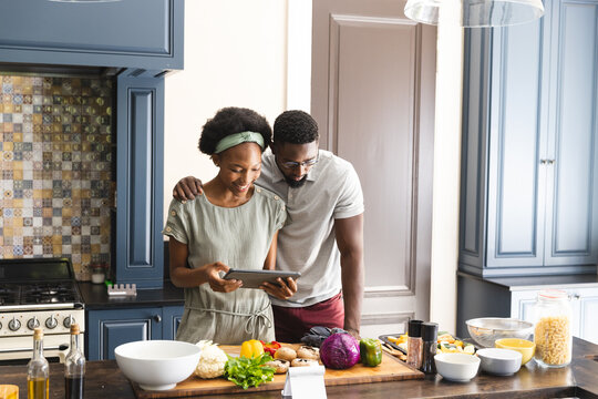 Happy african american couple preparing meal together using tablet in kitchen