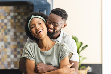 Portrait of happy african american couple embracing and laughing in kitchen