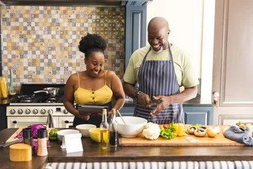 Tuinposter Happy senior african american couple preparing meal together, using tablet in kitchen © wavebreak3