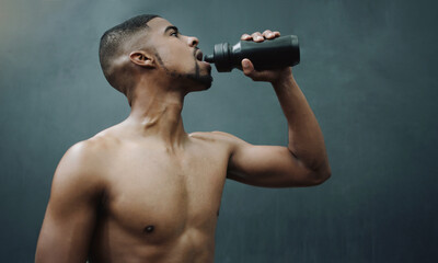 Naklejka na ściany i meble Fitness, man and drinking water on wall background after workout, exercise and training at a gym. Bottle, hydration and male relax after cardio, bodybuilding or challenge at sports center with space
