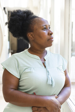 Thoughtful Senior African American Woman Standing Looking Out Of Window At Home