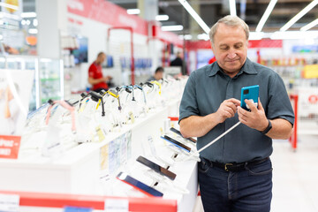 Mature man diligently choosing smartphone in hypermarket