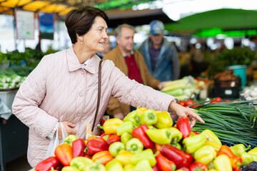 Mature casual female choosing fresh local organic vegetables for upcoming cooking at bazaar