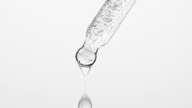 Closeup cosmetic serum fluid gel with bubbles from dropper, pipette over white