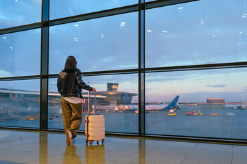 Travel.young woman at airport at window with suitcase waiting for plane, girl waiting for departure...