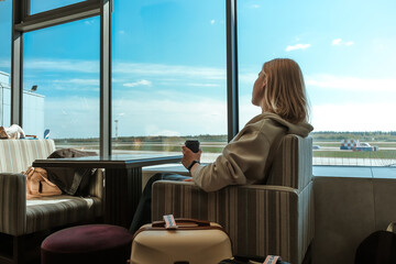 Travel.young woman at airport at window with suitcase waiting for plane, girl waiting for departure at the airport on your vacation. Uses a smartphone and drinks coffee