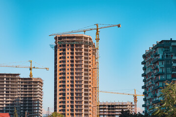 Fototapeta na wymiar Cranes building on construction site against blue sky. Industry of housing new buildings