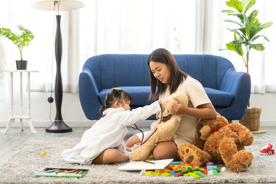 Portrait of enjoy happy love asian family mother and little asian girl smiling activity learn and skill brain training play with costume doctor toy examining heartbeat of teddy bear at home
