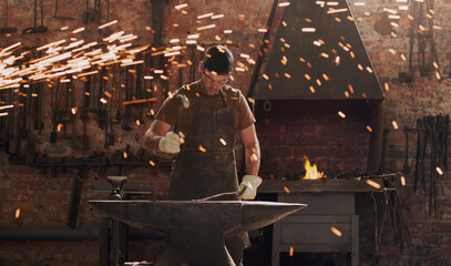 Hammer, anvil and fire with a man in a forge workshop for metal work manufacturing or production....