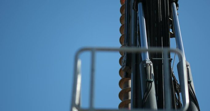Pneumatic components of heavy drilling machinery rises high into the sky. The camera pans down, eventually landing on handrails that are part of the large-scale construction equipment.